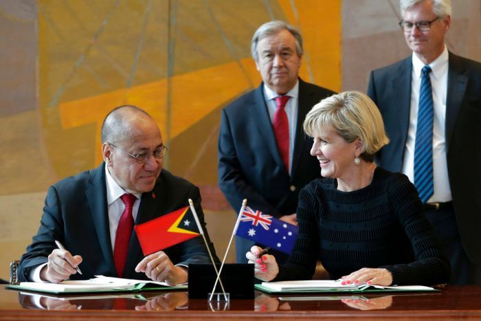 Agio Pereira and Julie Bishop sign paperwork in front of small East Timor and Australian flags. 