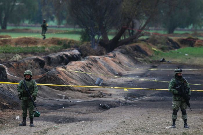 Soldiers guard the site where a gas pipeline exploded two days prior, the earth is scorched.