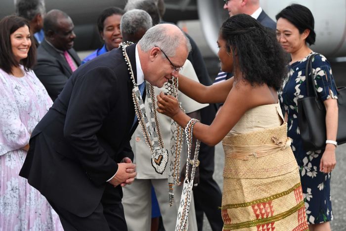 A woman in traditional clothing puts a large necklace on Scott Morrison. 