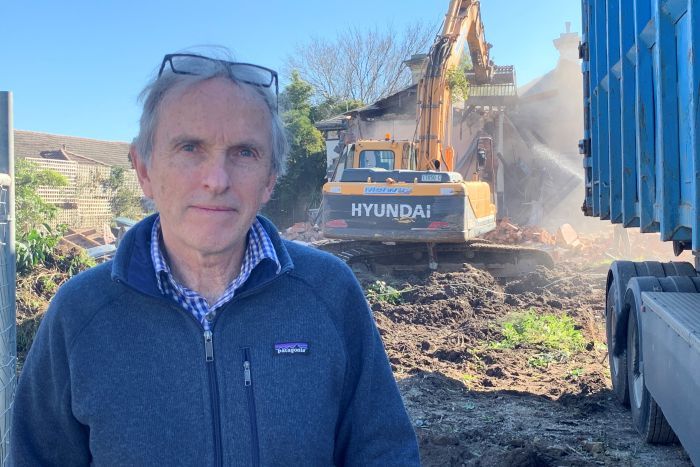 Hawthorn resident Andrew Sutherland looks at the camera as a bulldozer demolishes a house.